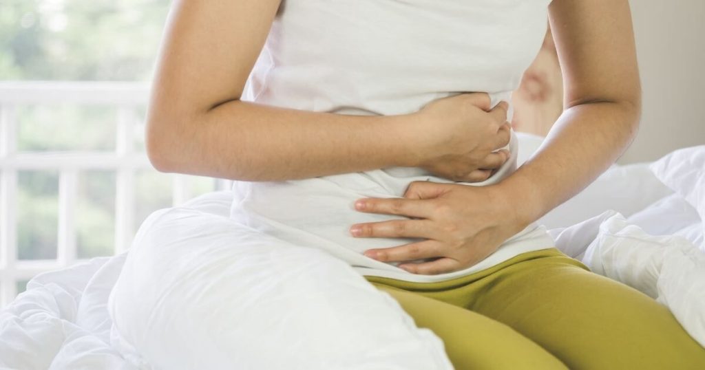 Person sitting on a bed holding their abdomen in pain