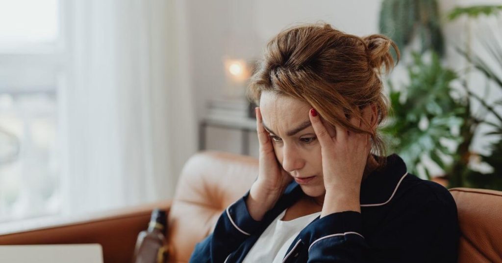 Woman sitting on a sofa holding her head, appearing stressed and overwhelmed