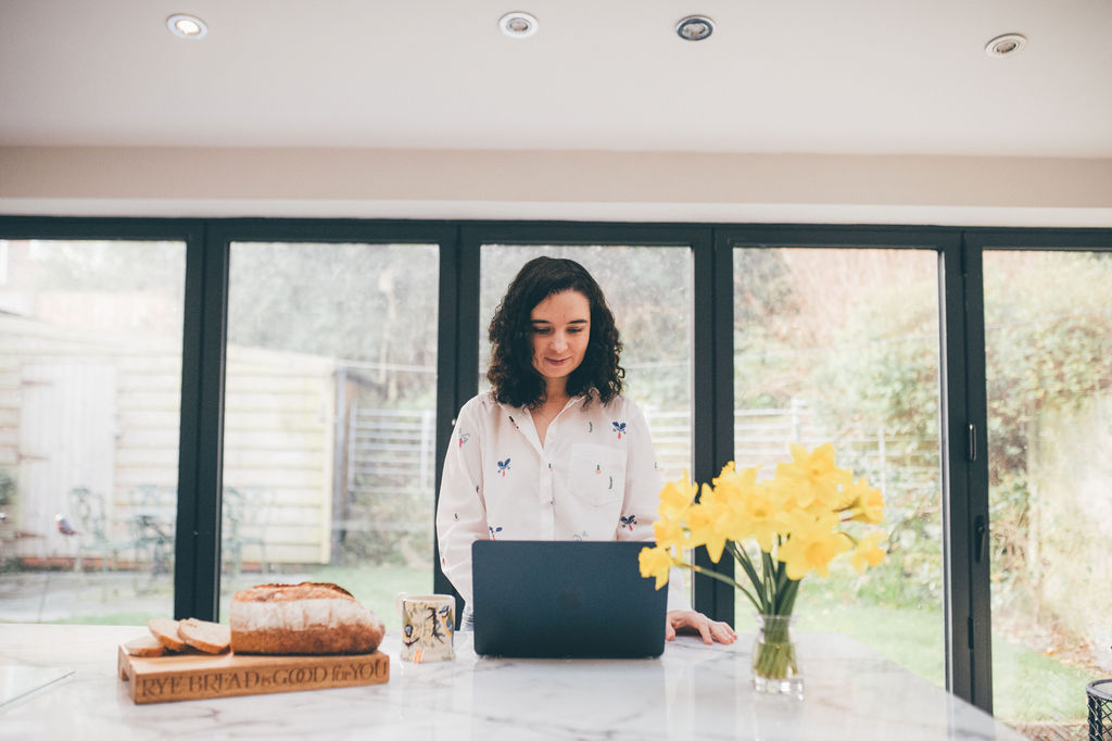 Woman working at a laptop near a bright window with yellow flowers, representing a calm, manageable daily routine