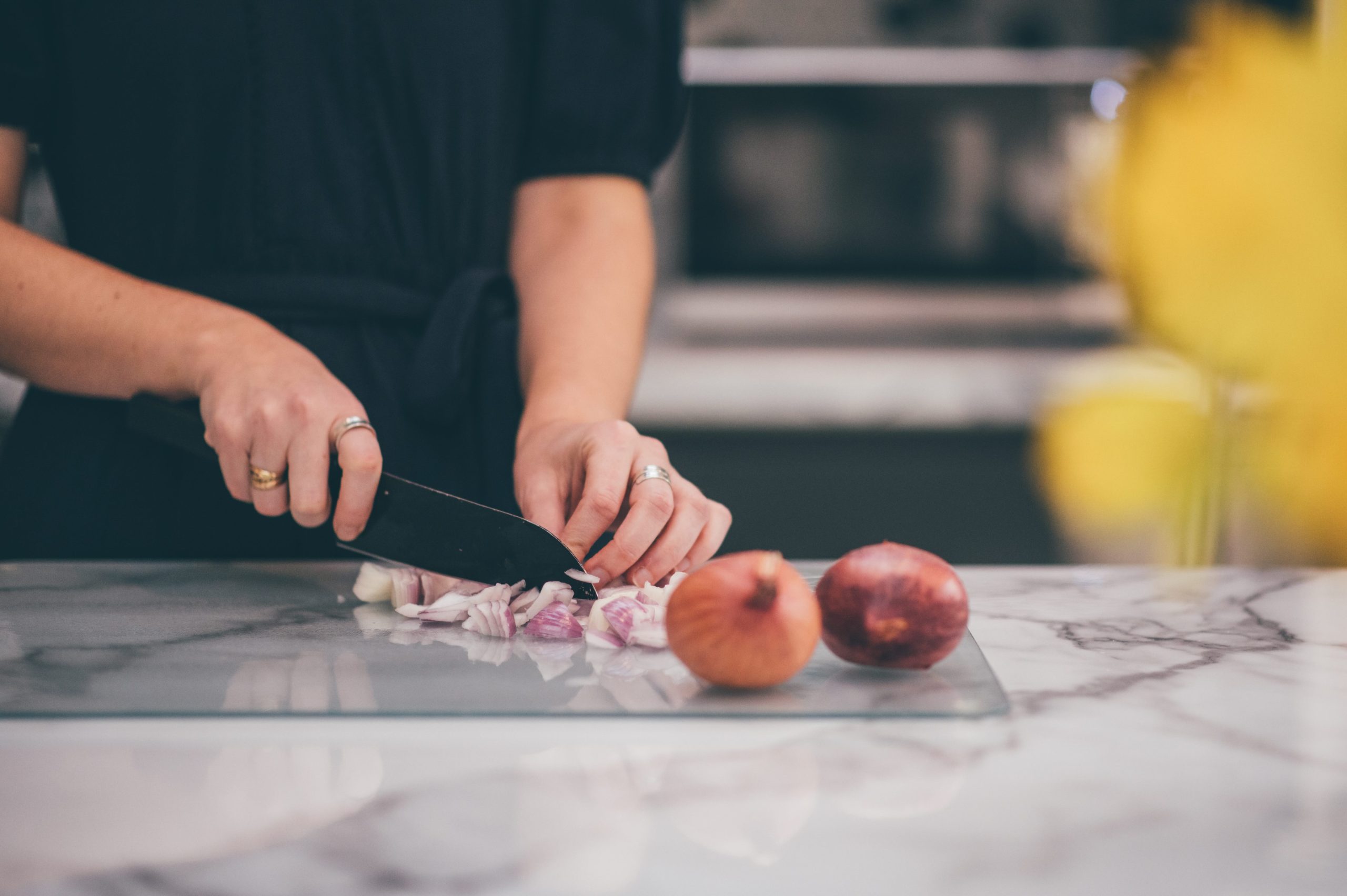 Hands chopping garlic and onions on a marble cutting board, representing whole food gut-friendly cooking